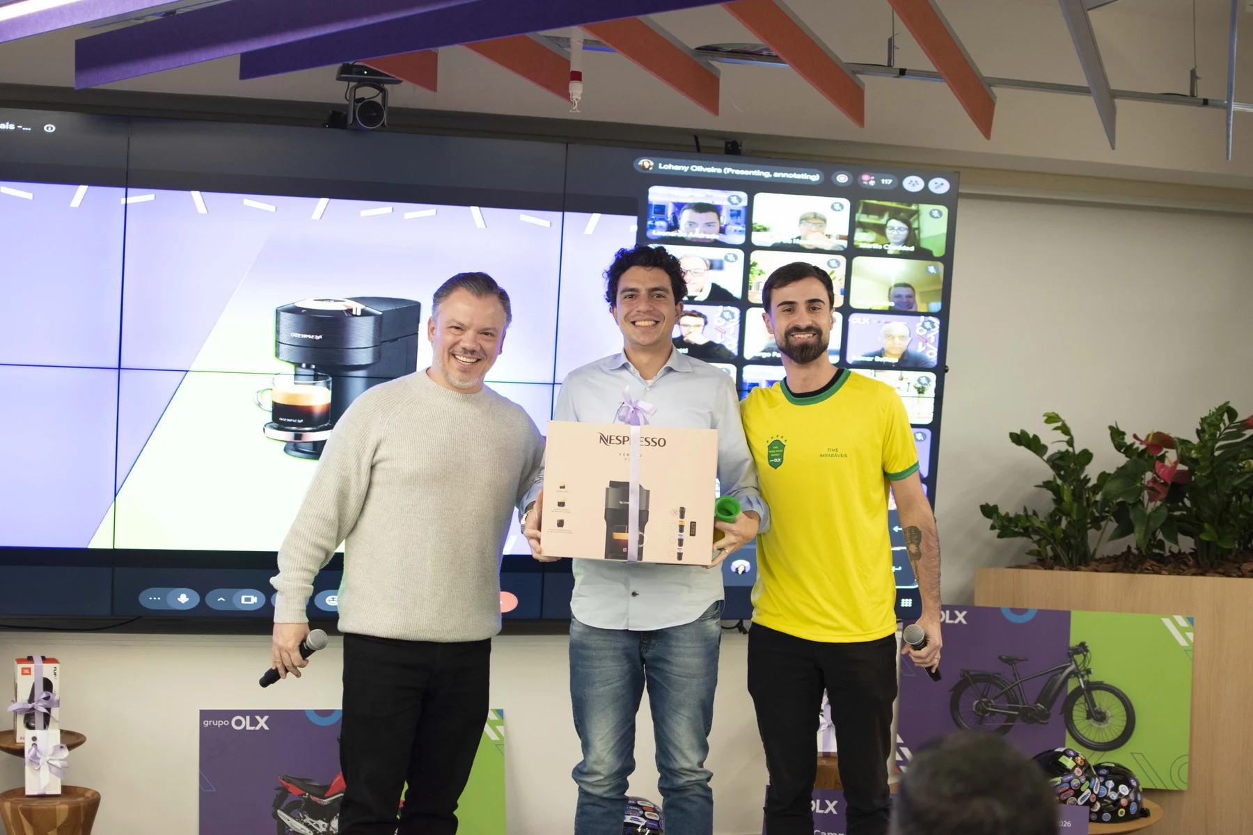 Participante com uma caixa de cafeteira, ao lado dos apresentadores no encontro OLX
